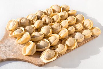 Homemade Siberian dumplings with meat filling on a wooden cutting board, on a light background. Making a delicious high-calorie Russian dish