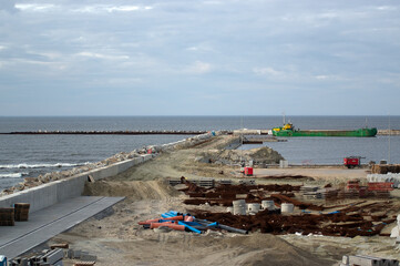 Plac budowy plaża falochron materiały budowlane betonowe bloczki i stalowe pręty zwały piasku.	
