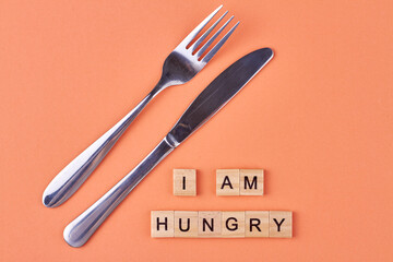 Flat lay composition from cutlery and wooden cubes with inscription I am hungry. Color background.