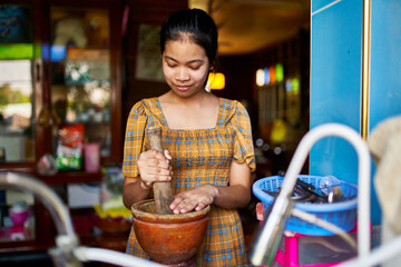 teenage thai girl using mortar and pestle in kitchen