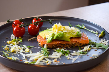 Homemade delicious roasted crisp sandwich with toast, salmon and avocado. Served on the side with Grana Padano or Parmigiano (Parmesan) cheese and Cherry Tomatoes.