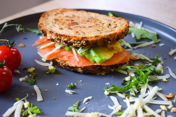Homemade delicious roasted crisp sandwich with toast, salmon and avocado. Served on the side with Grana Padano or Parmigiano (Parmesan) cheese and Cherry Tomatoes.