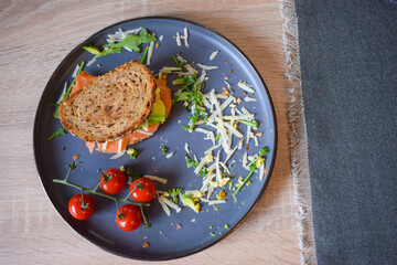 Homemade delicious roasted crisp sandwich with toast, salmon and avocado. Served on the side with Grana Padano or Parmigiano (Parmesan) cheese and Cherry Tomatoes.