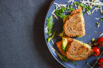 Homemade delicious roasted crisp sandwich with toast, salmon and avocado. Served on the side with Grana Padano or Parmigiano (Parmesan) cheese and Cherry Tomatoes.