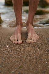 The guy stands on the sand barefoot. Legs close up. Sea. Ocean