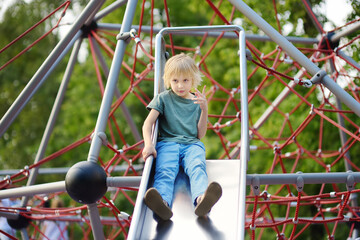 Cute little boy having fun on outdoor playground. Spring summer autumn active sport leisure for...
