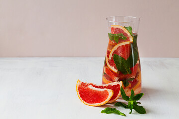 Glass jug of Cocktail grapefruit with fruits. fresh Grapefruit juice with green mint on beige background. grapefruit lemonade. Refreshing summer drinks. copy space.