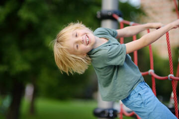 Cute perky preschooler boy having fun on outdoor playground. Spring or summer or autumn active...