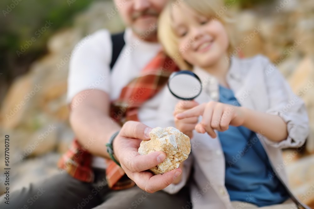 Wall mural cute schoolchild and his mature father hiking together on mountain and exploring nature. family watc