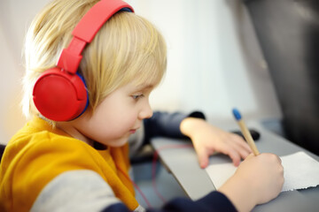 Fototapeta na wymiar Cute little boy traveling by an airplane. Child using player to listen a music or audiobook during the flight and drawing pictures. Entertainment for kids on a board of plane