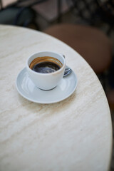 a white cup and a white saucer with coffee stands on the table, close-up
