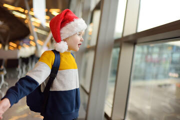 Little child wearing Santa Claus hat on background of an international airport. Preschooler boy is...