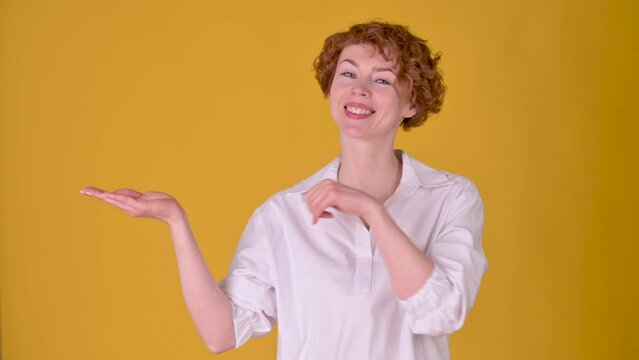 Young cheerful girl with red hair pointing empty place on her palm and smiling at the camera. Attractive woman showing empty space for commercial image. People lifestyle