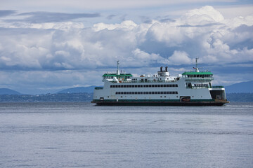 Fototapeta na wymiar A ferry hauls passengers and vehicles across Puget Sound on a sunny morning as a thick layer of clouds accumulate in the distance.
