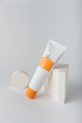 Cream tube mockup, cosmetics container template on white with concrete geometric decor. Face skin care, sea buckthorn extract