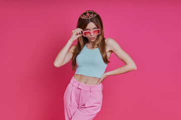 Playful young woman in funky crown standing against pink background