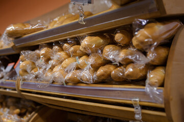 Loafs of wheat long bread in plastic packages on wooden shelves of supermarket, grocery department store, local shop.