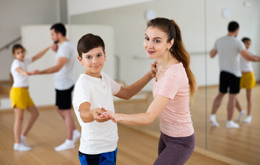 Young woman practicing active dance in pair with her tween son during family dance class