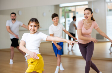Cheerful girl exercising in family group during dance class at dance studio