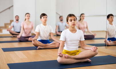 Fototapeta na wymiar Positive pre-teen girl performing yoga exercises with brother and parents at gym, family health concept