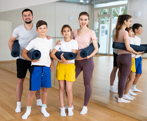 Smiling fit woman, man and teenage girl and boy posing with yoga mats before training at yoga studio