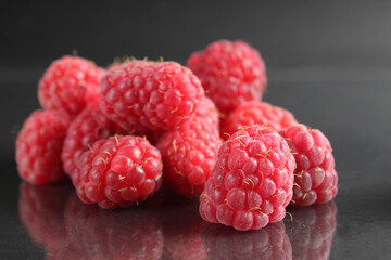 raspberries lie in a heap on a black background with a reflection. Vitamins seasonal berries freshness taste benefit. Raspberries for packaging labels