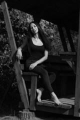 Beautiful slender barefoot woman in wooden gazebo in black and white