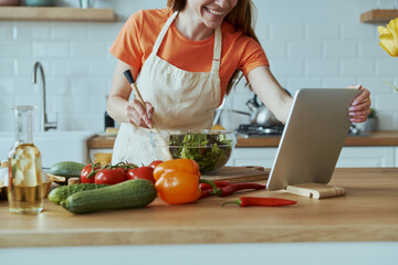 Close-up of young woman cooking and using digital tablet while standing at the domestic kitchen