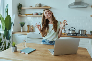 Happy young woman enjoying online shopping and using credit card while sitting at the kitchen
