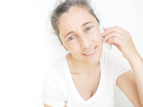 Forty Nine Year Old Woman In A White T-Shirt Against A White Background Talking On Her Cellphone