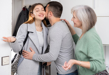 Woman came home after work trip, her husband and mother-in-law welcoming and embracing her at home.