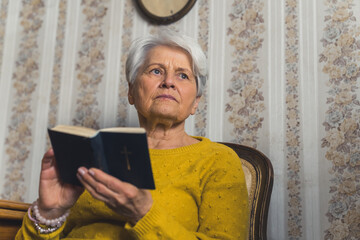 an old senior woman holding the Bible and thinking about the life medium closeup living room...