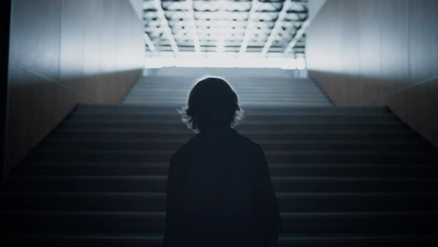 Teenager silhouette going upstairs alone on light. Teen student walk stairway.