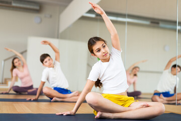 Fototapeta na wymiar Positive pre-teen girl performing yoga exercises with brother and parents at gym, family health concept