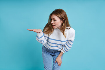 Attractive young woman gesturing something short while standing against blue background