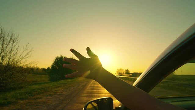 Free girl driver drives car, catches wind with her hand from car window. Young woman in front seat of car, sticking her hand out window, catching wind, glare of sun. Family, child traveling by car