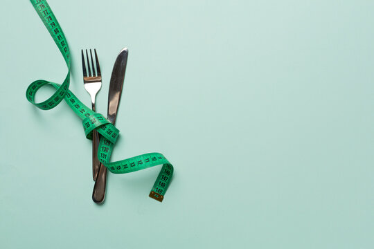 Green tape measure with cutlery on color background, top view