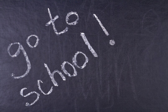 Handwritten inscription go to school on black chalkboard close up. Time for education concept.