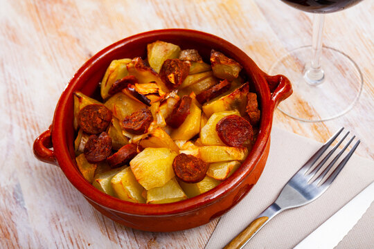 Appetizing oven-baked potato with sliced chorizo served in clay bowl