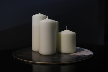 Fototapeta na wymiar three thick white candles on a tray in the dark