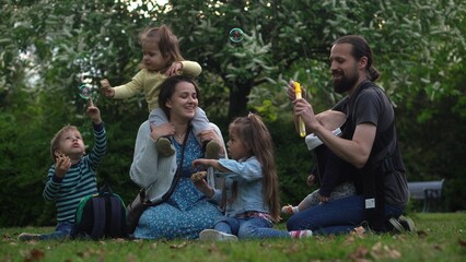 Happy family mother Father Three four Baby little siblings kids have fun blowing bubbles enjoying summer holidays in garden park. Smiling parents children spending leisure time together evening sunset