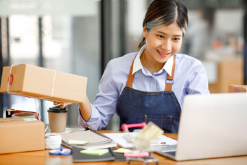 Young Asian entrepreneur SME woman checking product on stock take note with a laptop. Small business owner working at home. Check address on the parcel SME online start up freelance concept.