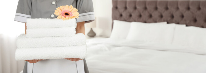 Chambermaid with stack of fresh towels in hotel room, closeup view with space for text. Banner...