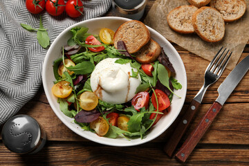 Delicious burrata salad with colorful cherry tomatoes, croutons and arugula served on wooden table, flat lay