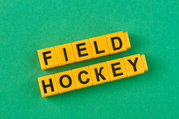 The inscription field hockey written on yellow cubes against green background. Type of sport.