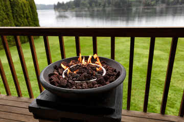 Burning gas firepit on outdoor home deck with lake and woods in the background