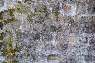 Old stone wall with moss growing on it creates abstract grungy textured background