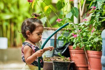 little latin girl taking care of the flora. girl watering the plants in her garden. Girl playing with water.