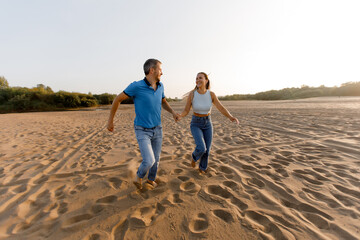 A happy young couple in love is having fun on the beach, running towards the sun, carelessness and happiness. Vacation concept and happy weekend