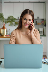 Portrait of young woman answering mobile call during online work on laptop